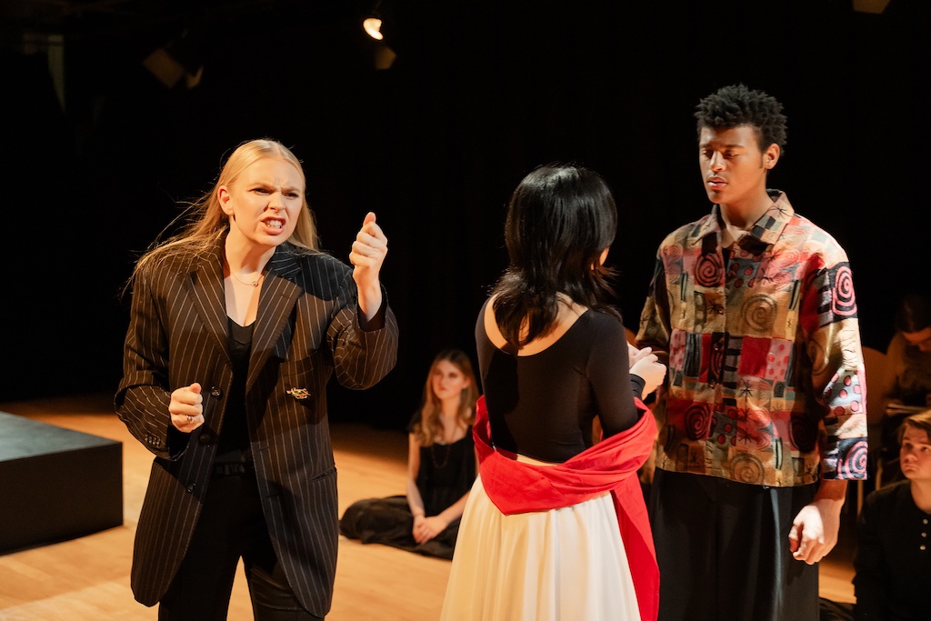 An actor angrily gestures toward two other actors who are facing each other in mid-performance during the final presentation of The Winter's Tale.